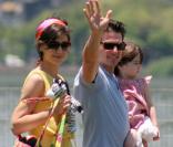 Tom Cruise acena para fotógrafo enquanto leva a filha, Suri, para passear durante visita ao Brasil. Katie Holmes carrega os brinquedos da menina, em fevereiro de 2009