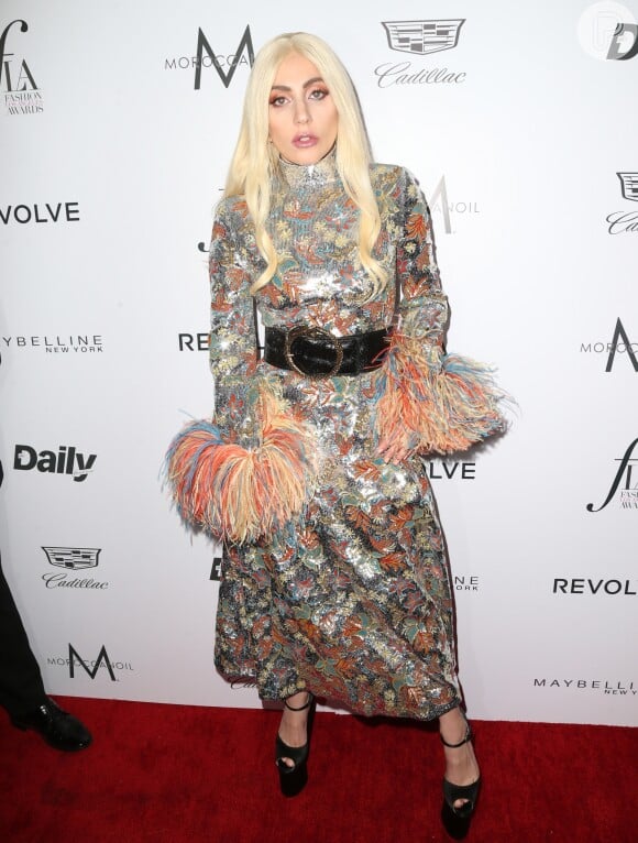 Lady Gaga usou vestido da grife Saint Laurent metalizado com penas coloridas na borda das mangas, que escondiam as mãos da cantora
