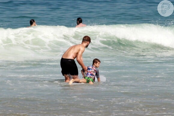 Rodrigo segura o filho em cima da prancha de surfe