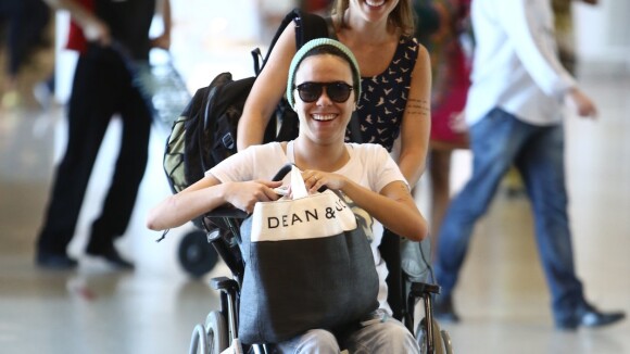 Maria Gadú, de cadeira de rodas, é empurrada pela mulher, Lua Leça, em aeroporto