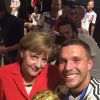 Lukas Podolski faz selfia com a chanceler da Alemanha, Angela Merkel, segurando a taça no vestiário do Maracanã