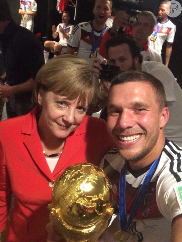 Lukas Podolski faz selfia com a chanceler da Alemanha, Angela Merkel, segurando a taça no vestiário do Maracanã