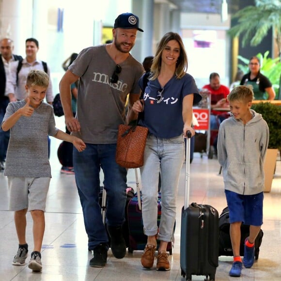 Fernanda Lima e Rodrigo Hilbert aparecem sorridentes em aeroporto e Francisco faz sinal para fotógrafo