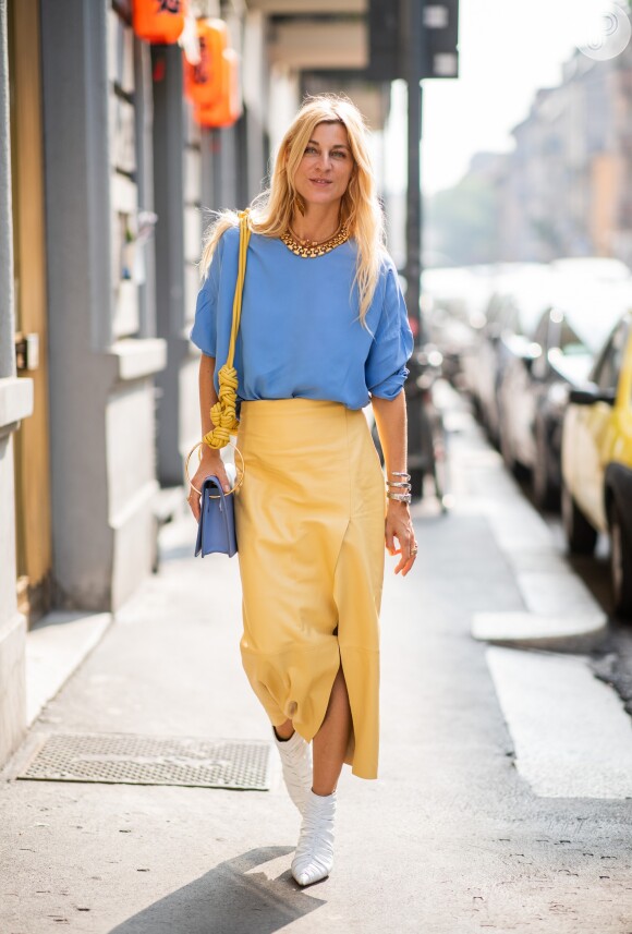 A saia midi amarela faz um duo solar com a alça da bolsa e o contraste com o azul da blusa e as botas brancas