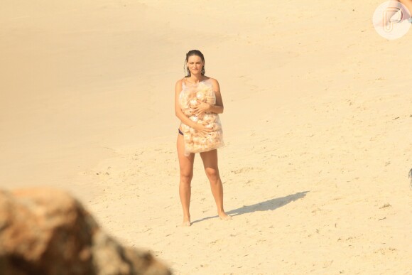 De biquíni, Débora Nascimento grava cenas da novela 'Verão 90' agarrada a um saco de biscoito de polvilho na praia do Arpoador, no Rio
