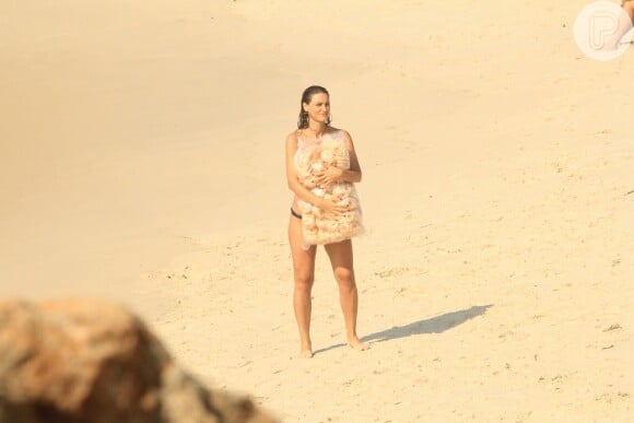 Na praia, Débora Nascimento aguarda orientações segurando um saco de bicoitos na praia