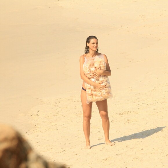 Na praia, Débora Nascimento aguarda orientações segurando um saco de bicoitos na praia
