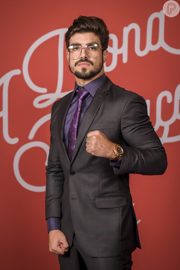 Caio Castro de terno cinza, camisa e gravata roxas e óculos de grau