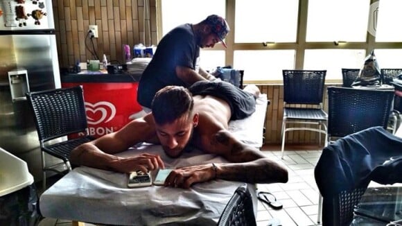 O jogador, que passa as festas de final de ano no Brasil, se distrai com o celular enquanto é tatuado por Filipe Genesi