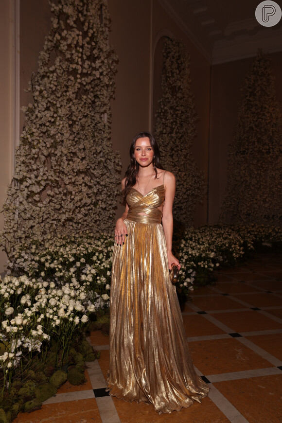 Carol Adriano veste vestido longo dourado como convidada do casamento de Paula de Aziz