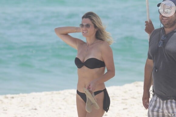 Flávia Alessandra grava de biquíni tomara que caia em praia carioca