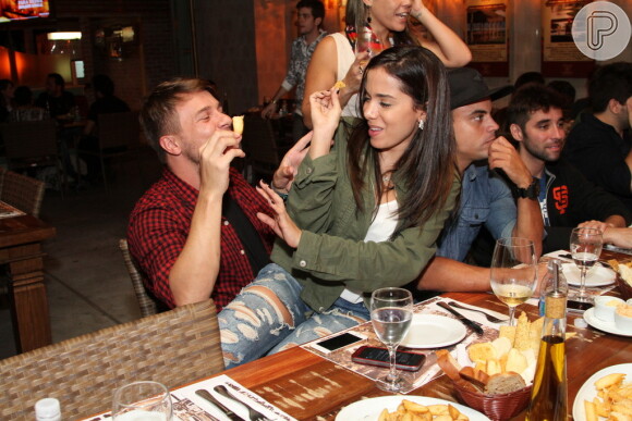 Anitta senta no colo de amigo e brinca de colocar comida em sua boca