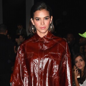 Bruna Marquezine apostou em conjunto com jaqueta e minissaia de vinil, na cor vinho, para acompanhar desfile