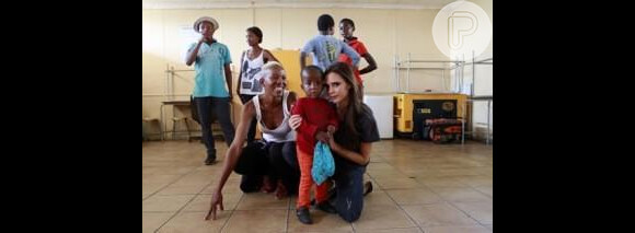 Victoria Beckham posa ao lado de criança na instituição criada pelo cantor em prol dos portadores do vírus da Aids
