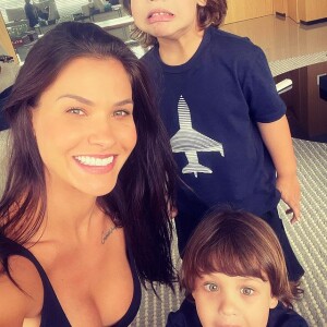 Andressa Suita sorri para foto com os filhos, e Gusttavo Lima aparece no reflexo de um espelho
