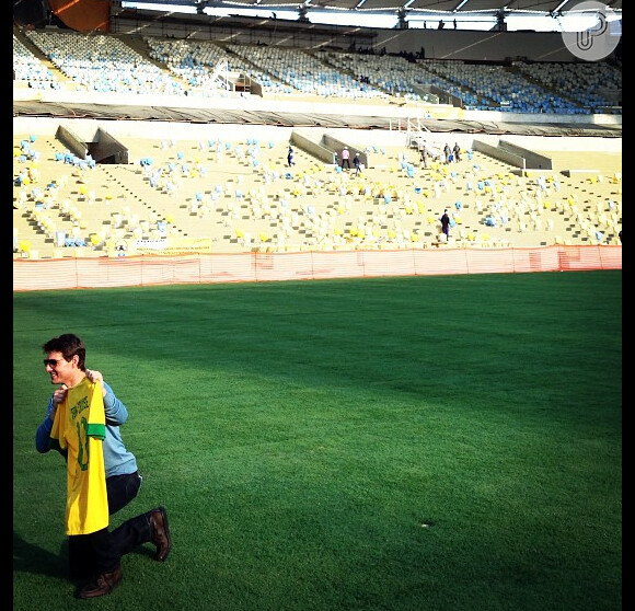 Com a camiseta da seleção brasileira nas mãos, Tom Cruise se ajoelha no gramado do Maracanã