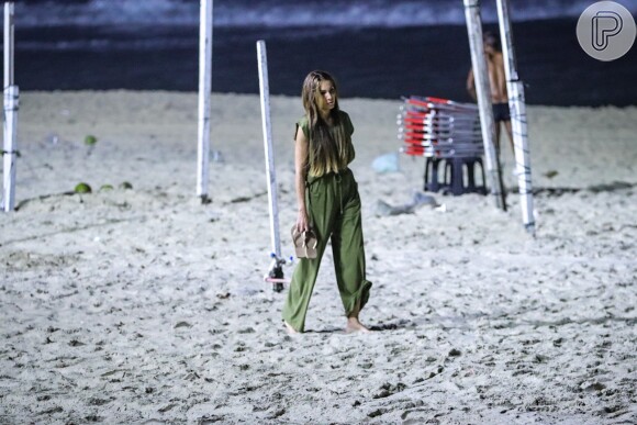 De macacão verde, Patricia Poeta tirou o chinelo para caminhar pela areia da praia