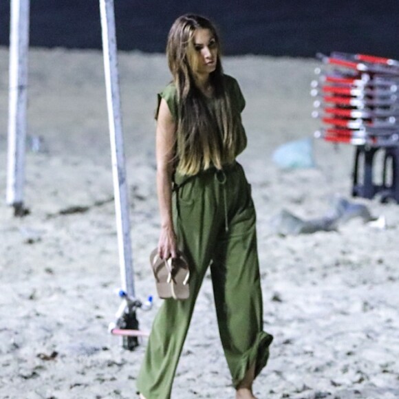 De macacão verde, Patricia Poeta tirou o chinelo para caminhar pela areia da praia