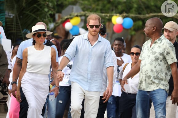 Agora, a camisa que Meghan Markle usou era sem mangas, de um tecido que parece linho, de cor clara, e combinou à uma peça inferior do mesmo tom.