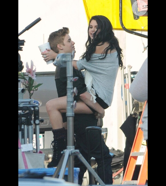 Justin Bieber segura  Selena Gomez no colo no set de filmagem de um clip do cantor.
