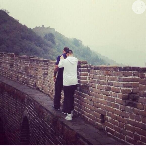 Justin Bieber anda na beirada da Grande Muralha da China encostado em uma dos seguranças