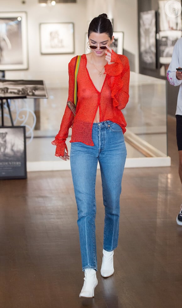 Kendall Jenner usou a blusa transparente com calça jeans de cintura alta, ankle boots brancas e óculos escuros