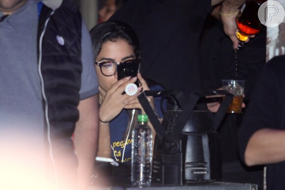 Anitta, sem maquiagem, ficou no celular o tempo todo durante o evento do namorado, Thiago Magalhães