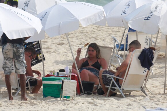 Marília Mendonça conversa com amigos na praia enquanto belisca um queijo coalho