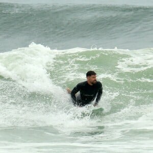 Cauã Reymond pratica surfe em dia nublado no Rio de Janeiro