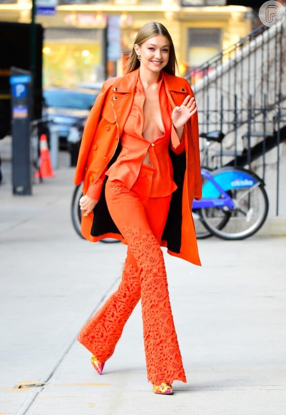 Gigi Hadid em look completo: all orange, decotão, calça flare e high heels.