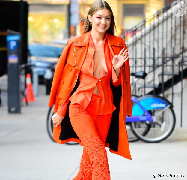 Gigi Hadid em look completo: all orange, decotão, calça flare e high heels.