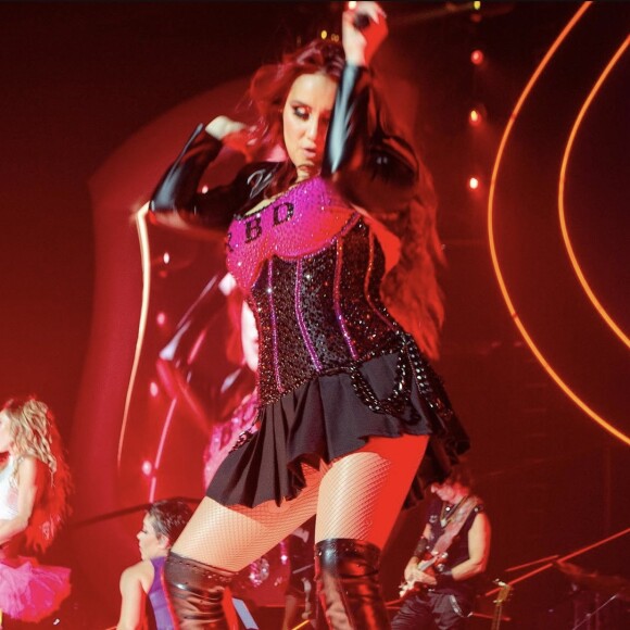 Corset preto com brilho: Dulce Maria está usando bastante minisaias, corsets e até uma blusa bordada com o nome do RBD nos shows