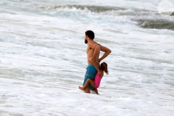 Na água do mar, Cauã Reymond segura a filha, Sofia, pelos braçõs