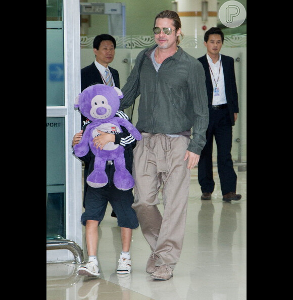 Brad Pitt caminha ao lado do filho Pax, que se esconde atrás de um urso de pelúcia