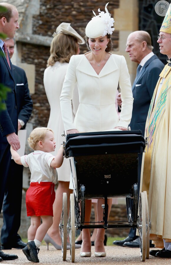 Príncipe George se apoia no carrinho para ver a irmãzinha, Charlotte, observado por Kate Middleton e príncipe William batizam