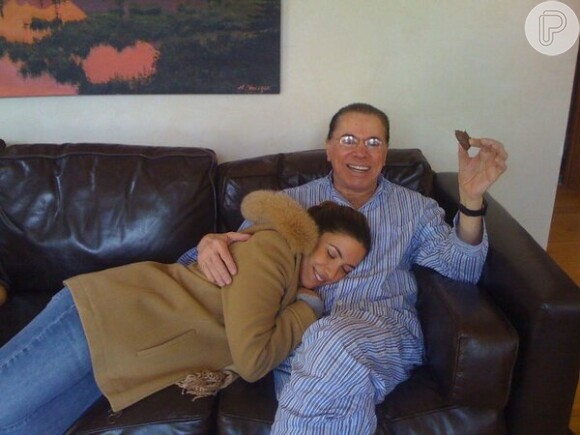Silvio Santos dá colo para a filha Patricia Abravanel enquanto assiste televisão de pijamas e comento biscoito, em imagem postada por Nelson Rubens no Twitter