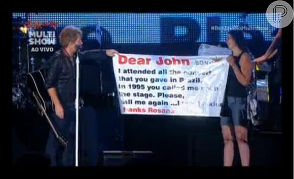 Bon Jovi chama a fã ao palco e lê o cartaz: 'Em 1995 você me chamou ao palco. Me chame novamente. Eu quero um beijo'