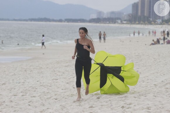  A atriz corre na areia com um paraquedas amarrado em sua cintura