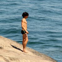 André Gonçalves salta de pedra para mergulhar no mar, em praia no Rio