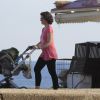 Larissa Maciel caminha empurrando o carrinho da filha, Milena, em praia do Rio