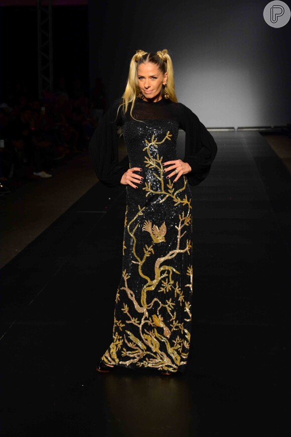Adriane Galisteu usou vestido longo preto e dourado no desfile do estilista Walério Araújo, em São Paulo