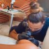 Anitta exibe duas tatuadoras em cada perna, ao mesmo tempo
