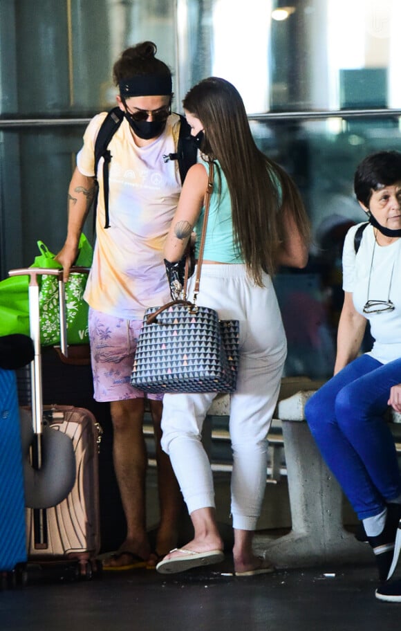 Namorada de Whindersson Nunes, Maria Lina usa calça branca, top e chinelo para desembarcar no Brasil