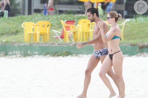 A atriz impressiona pela boa forma de biquíni em uma praia carioca na companhia de um amigo