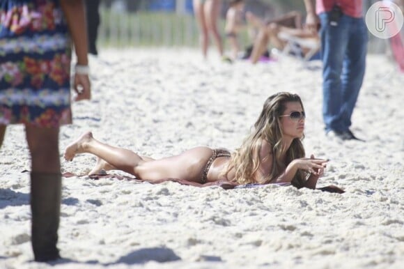 Fernanda Souza mostra o corpão deitada na areia da praia da Barra, RJ, durante gravação