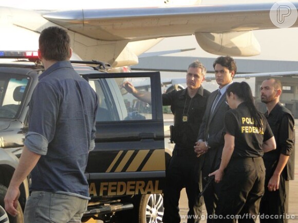 Hélio (Raphael Viana) foi preso dentro de um avião, tentando sair do país com documentos falsos, em 'Flor do Caribe'