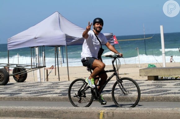 Em passeio de bicicleta na orla da praia, o ator cumprimenta o paparazzi com simpatia