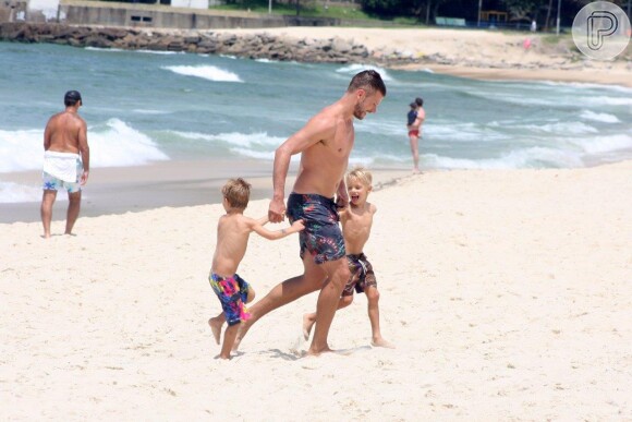 Rodrigo Hilbert caminha na areia com os filhos gêmeos João e Francisco