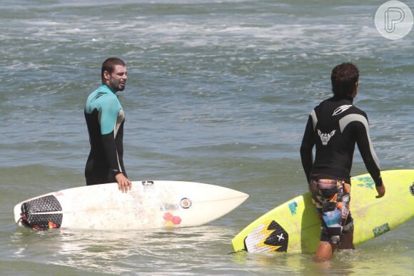 Cauã Reymond surfa na companhia de um amigo na praia da Barra da Tijuca, na Zona Oeste do Rio de Janeiro, em 20 de fevereiro de 2014