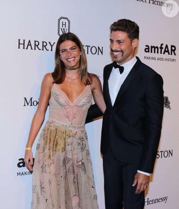 Cauã Reymond e Mariana Goldfarb posam sorridentes pelo tapede vermelho do baile amfAR